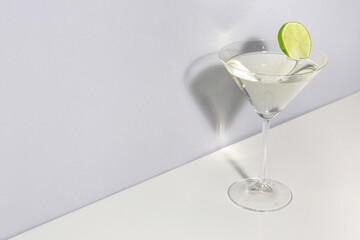 Glass of martini with lime on light background
