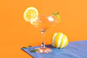Glass of tasty martini and lemon on orange background