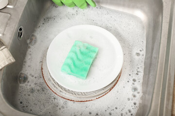 Plates with cleaning sponge in sink, closeup