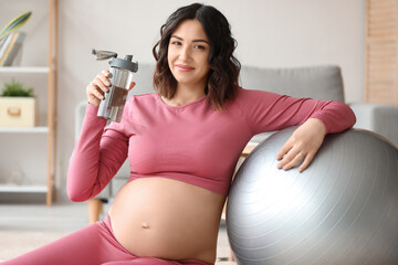 Sporty pregnant woman with bottle of water and fitball at home