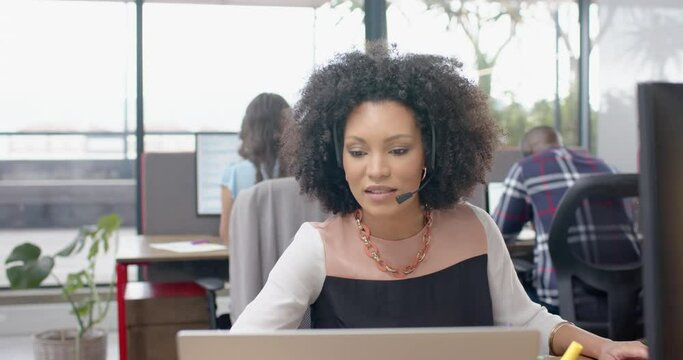 African american woman talking on phone headset and using laptop at office