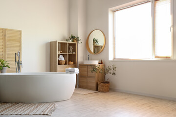 Interior of light bathroom with white sink, shelving unit and bathtub