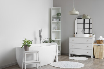 Fototapeta na wymiar Interior of light bathroom with white sink, bathtub, shelving unit and houseplants