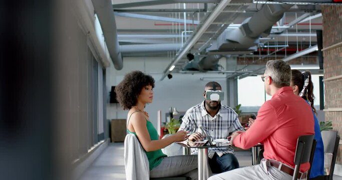 African american businessman wearing vr headset while colleagues watching him at office