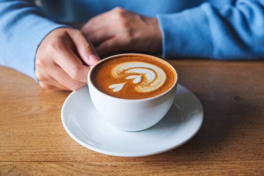 Closeup image of a woman holding a cup of latte coffee on wooden table