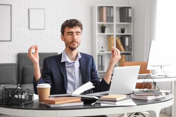 Fototapeta premium Young businessman meditating at table in office
