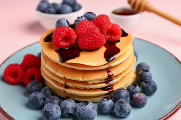 Plate with sweet pancakes and berries on pink background, closeup