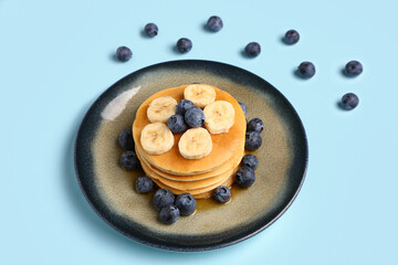 Plate with sweet pancakes, banana and blueberry on blue background