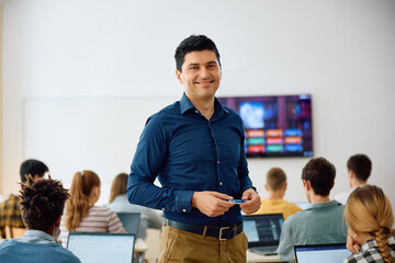 Happy teacher during computer class at high school looking at camera.