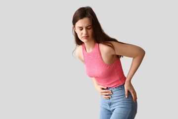Young woman having menstrual cramps on light background