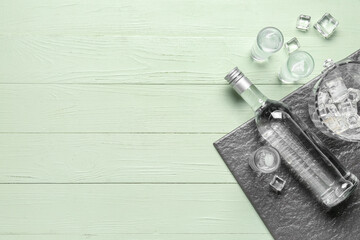 Bottle and glasses of cold vodka on green wooden background