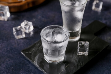 Board with shots of vodka on dark table