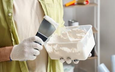 Young man with putty knife and plaster working at home, closeup