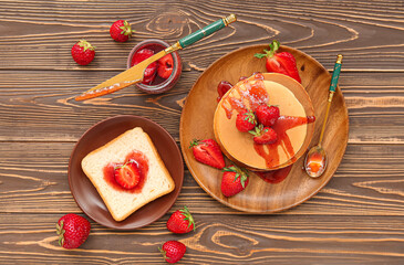 Plates of tasty pancakes and toast with sweet strawberry jam on wooden background