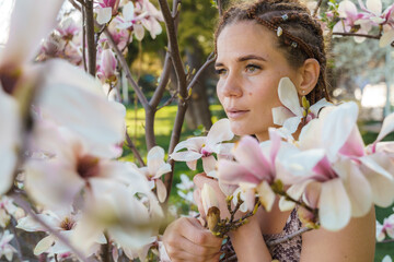 Obraz premium Magnolia flowers. Happy woman enjoys by blooming magnolia tree and sniffs it flowers with closed eyes in spring garden. Portrait.