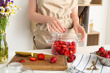 Woman preparing sweet strawberry jam at table in kitchen, closeup