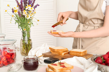 Woman preparing tasty toasts with sweet strawberry jam at table in kitchen