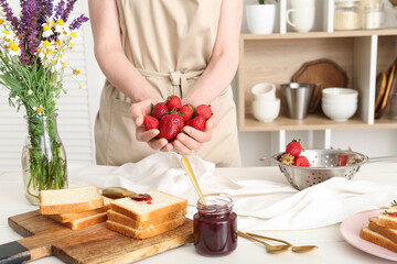 Woman holding fresh strawberries for preparing sweet jam at table in kitchen, closeup