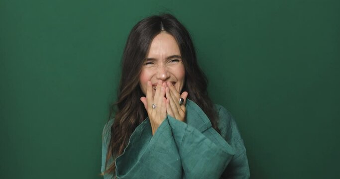 Happy joyful young woman wear green dress laughing out loud after hearing ridiculous anecdote, funny joke, feeling carefree amused, positive lifestyle, cover her mouth isolated on green background.