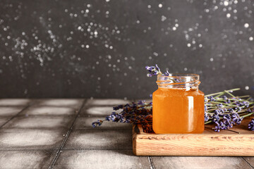 Wooden board with jar of sweet lavender honey and flowers on grey tile table