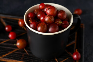 Cup with fresh gooseberries on black background