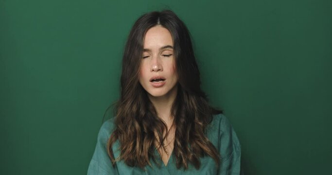 Serious brunette curly woman placing finger hand on lips, shh gesture, be quiet, silence, isolated green background. Negative facial expression, sign, emotion, feelings, body language.