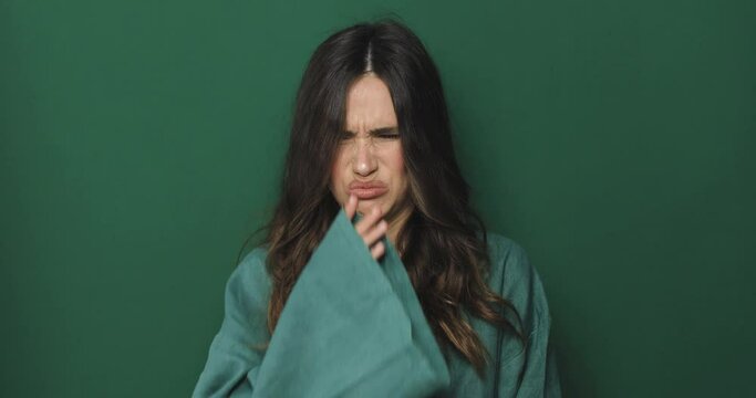 Disgusting odour. Discontent brunette curly woman frowning face, smells something awful, feeling aversion, green studio background. Girl face with aversion dislikes something unpleasant.