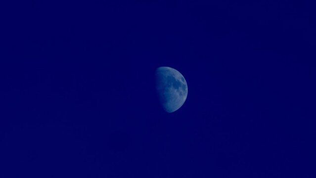 Close up of half moon with dark navy blue indigo clear sky background at night, moon light shining, telephoto lens 4k slow motion footage. High quality 4k footage