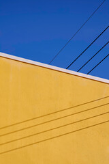 Colorful minimal architecture background. Diagonal pattern of the old yellow building wall with light and shadow of electric cable lines on surface against blue clear sky in vertical frame