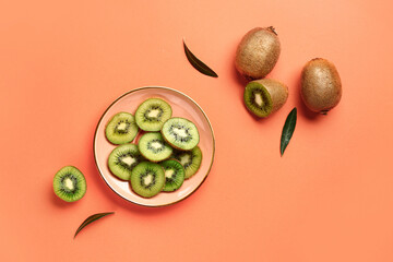 Plate with slices of fresh kiwi and leaves on orange background