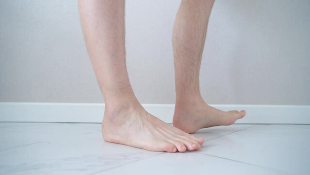 Close-up of men's feet barefoot on a tiled floor. Man walking on tiled white floor.