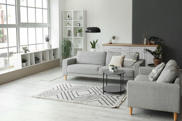 Interior of light living room with cozy grey sofas, coffee table and big window