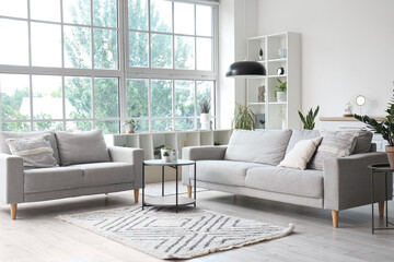 Interior of light living room with cozy grey sofas, coffee table and big window