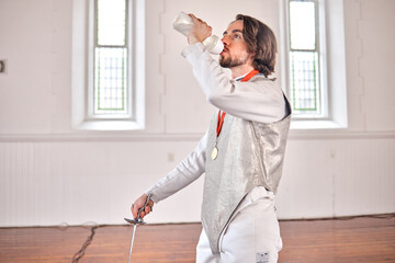 Fencing, sports and man drinking water after training, fitness or workout with sword in club....