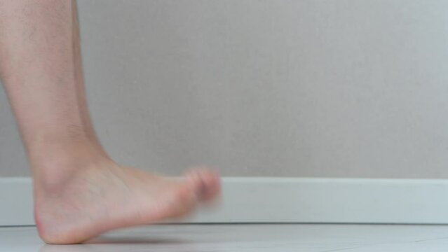 Close-up of men's feet barefoot on a tiled floor. Man walking on tiled white floor.