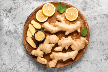 Wooden board with fresh ginger roots, sliced lemon and bowl of dried powder on grey background