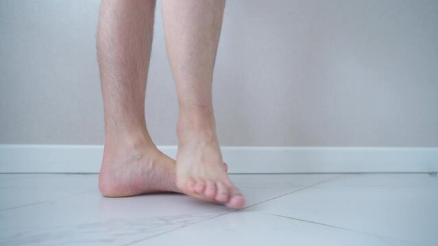 Close-up of men's feet barefoot on a tiled floor. Man walking on tiled white floor.