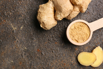 Fresh ginger root and wooden spoon with dried powder on dark background
