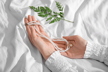 Female hands with beautiful pearl necklaces and plant branch on white cloth