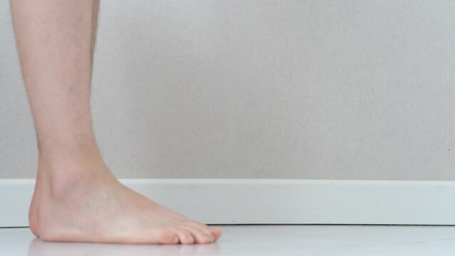 Close-up of men's feet barefoot on a tiled floor. Man walking on tiled white floor.