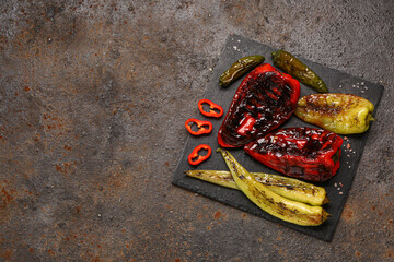 Board with different grilled peppers on dark background