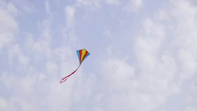 A multi-colored kite flying high in the sky under the gusts of wind.