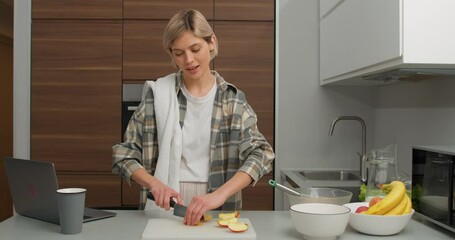 charming female blogger standing in kitchen, talking about fresh food ingredients on camera cutting apple making salad pie cake dessert filming for vlog Slow motion Housewife broadcasting live video - Powered by Adobe