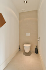 a white toilet in a room with beige walls and floor tiles on the wall, there is a lamp above it