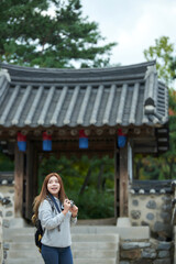 A young woman wearing a camera and taking pictures while traveling to tourist attractions with traditional Korean houses