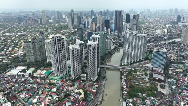 Manila cityscape at river banks aerial. Downtown area with cottages, skyscrapers, buildings. Urban Philippines city scape with streets and roads. Town drone shot. Poor Homes Along Rich Skyscrapers.