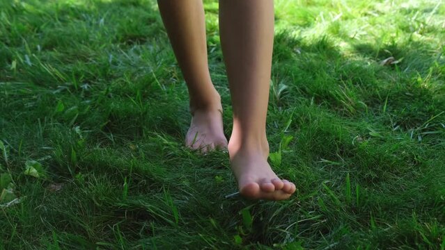 legs of a teenage girl barefoot walking towards the camera, stepping on green grass or lawn, front view