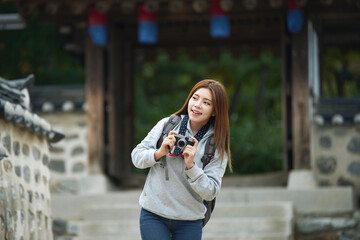 A young woman wearing a camera and taking pictures while traveling to tourist attractions with traditional Korean houses