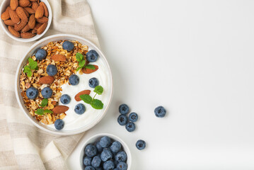 Granola with yogurt, blueberries and almond in bowls on a white background top view with copy space