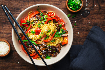Stir fry noodles with vegetables: paprika, champignons, chives and sesame seeds in ceramic bowl....